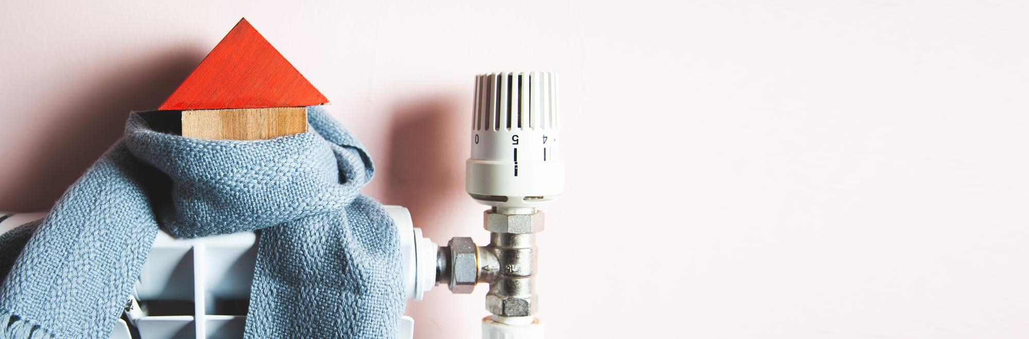 Un chauffage performant et bien entretenu pour un confort durable après le désembouage Radiateur avec thermostat et petite maison en bois entourée d’une écharpe bleue, symbole d’un chauffage efficace et économique après désembouage